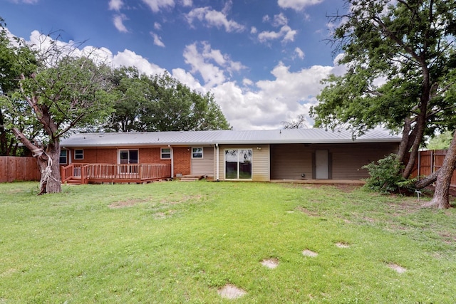 back of house with metal roof, fence, brick siding, a lawn, and a deck