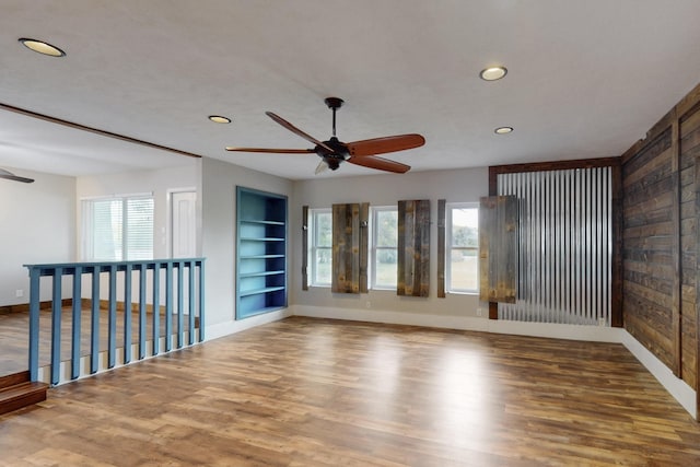 empty room with baseboards, recessed lighting, built in shelves, wood finished floors, and ceiling fan