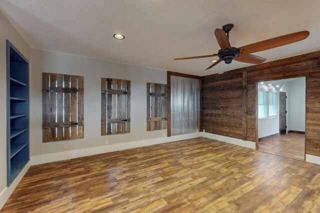 unfurnished room with wooden walls, wood finished floors, and ceiling fan
