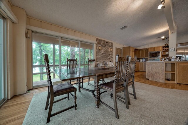 dining space featuring light wood-style flooring, a textured ceiling, lofted ceiling, and visible vents