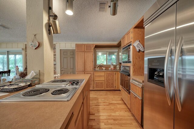 kitchen featuring a textured ceiling, light wood-type flooring, light countertops, appliances with stainless steel finishes, and visible vents