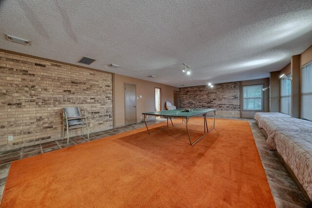 recreation room featuring brick wall, a wood stove, a textured ceiling, and visible vents