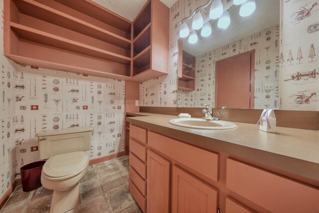 bathroom featuring toilet, vanity, wallpapered walls, and baseboards