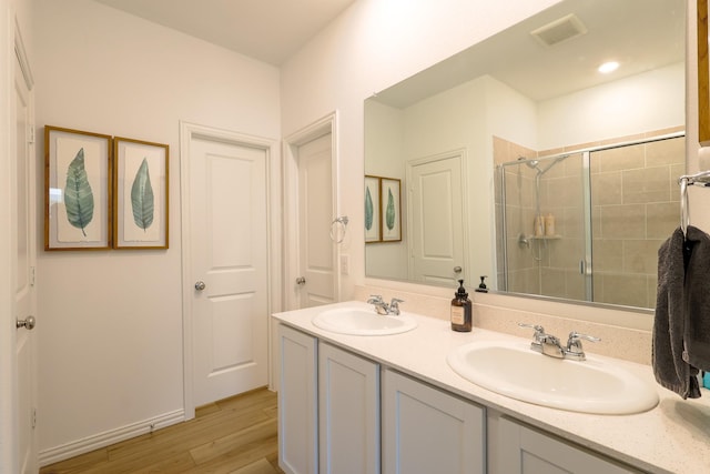 bathroom with wood finished floors, a sink, a shower stall, and double vanity