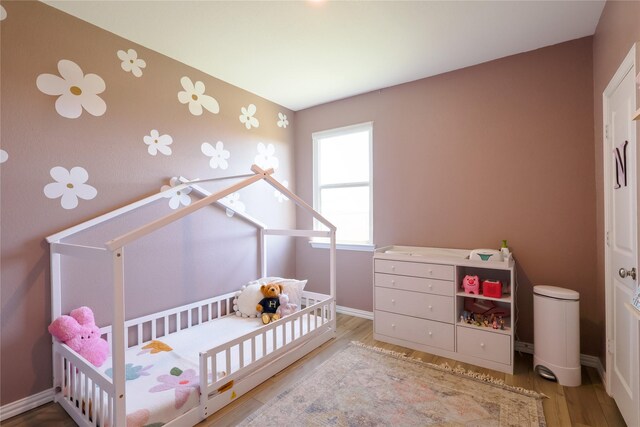 bedroom with a crib, baseboards, and wood finished floors