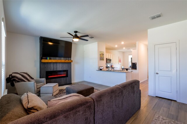 living room featuring wood finished floors, ceiling fan, a fireplace, visible vents, and recessed lighting