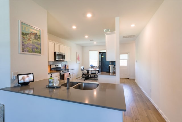 kitchen with a peninsula, dark countertops, visible vents, white cabinetry, and appliances with stainless steel finishes