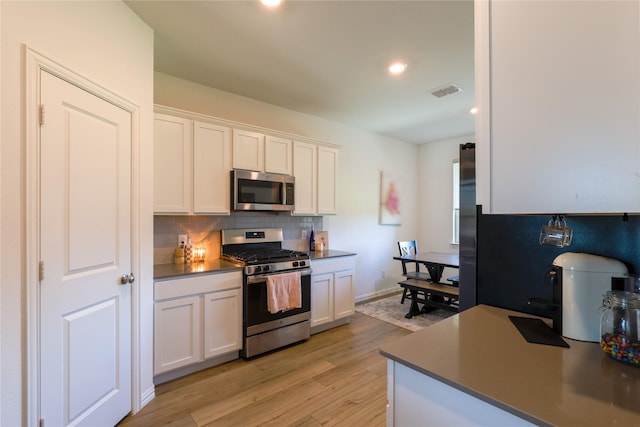 kitchen featuring white cabinets, visible vents, decorative backsplash, light wood-style flooring, and appliances with stainless steel finishes