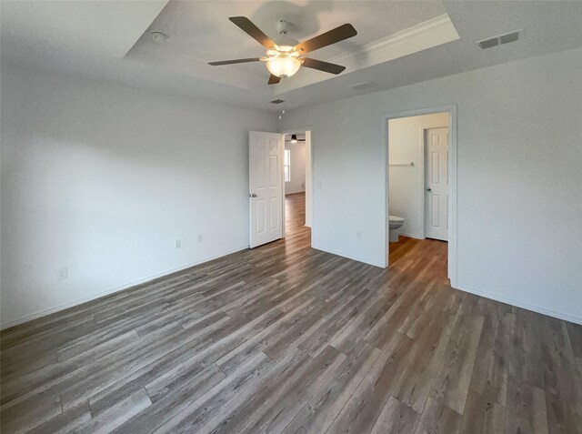 unfurnished bedroom featuring connected bathroom, visible vents, a tray ceiling, baseboards, and dark wood finished floors