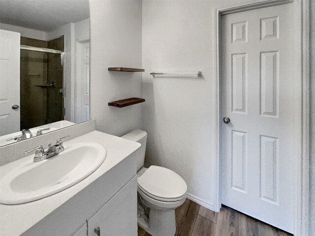 bathroom with toilet, vanity, a shower stall, and wood finished floors