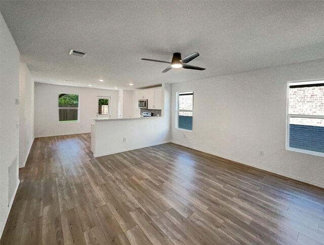 unfurnished living room featuring dark wood-type flooring, visible vents, and plenty of natural light
