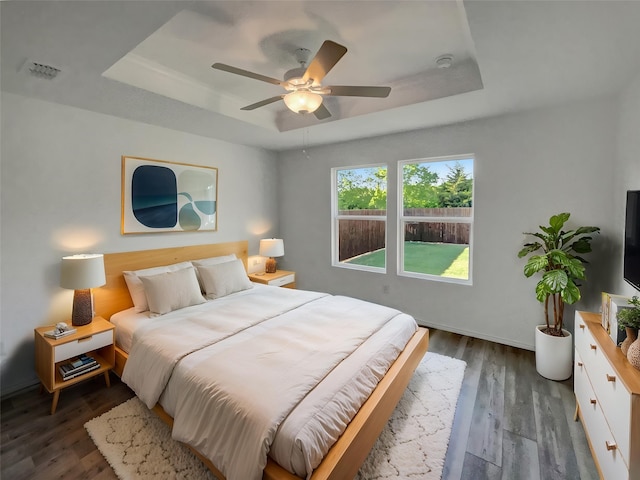 bedroom featuring dark wood-type flooring, a tray ceiling, and baseboards