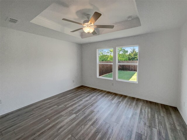 empty room featuring a raised ceiling, wood finished floors, visible vents, and ceiling fan