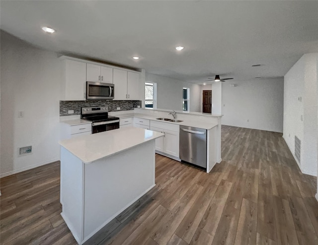 kitchen featuring appliances with stainless steel finishes, dark wood-style flooring, a sink, white cabinetry, and a peninsula