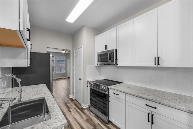 kitchen featuring wood finished floors, white cabinetry, a sink, backsplash, and stainless steel appliances