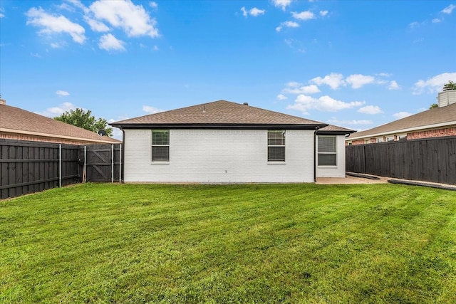 rear view of house featuring a patio, a fenced backyard, roof with shingles, brick siding, and a lawn