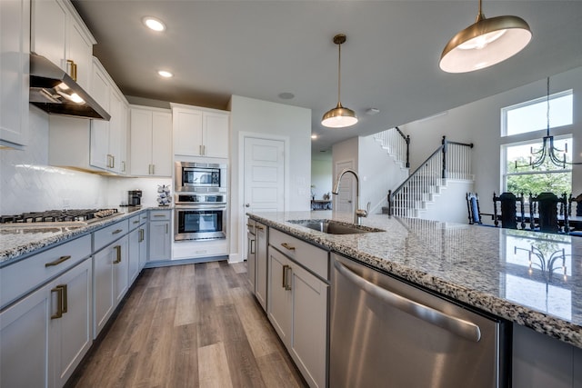 kitchen featuring a sink, pendant lighting, stainless steel appliances, under cabinet range hood, and dark wood-style floors