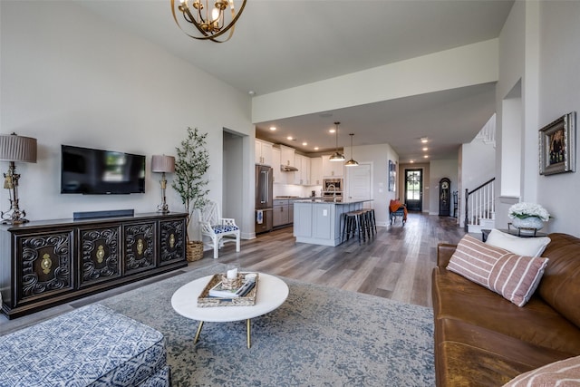 living room featuring baseboards, a towering ceiling, a notable chandelier, wood finished floors, and stairway