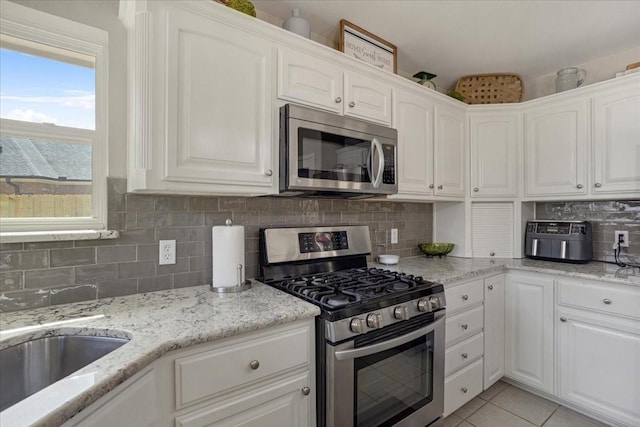 kitchen with white cabinets, light tile patterned flooring, backsplash, light stone counters, and appliances with stainless steel finishes