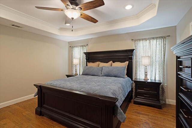 bedroom with wood finished floors, visible vents, ornamental molding, and a tray ceiling