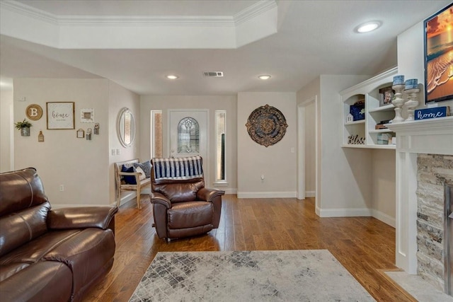 living room with ornamental molding, wood finished floors, visible vents, and a stone fireplace
