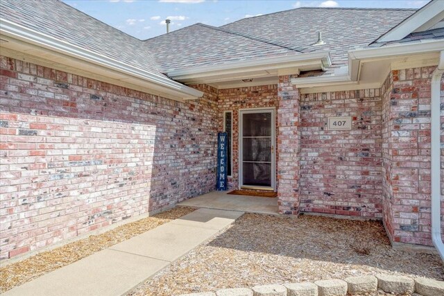 doorway to property with roof with shingles and brick siding