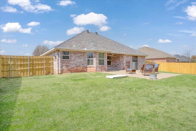 rear view of property with brick siding, a patio area, a lawn, a fenced backyard, and roof with shingles