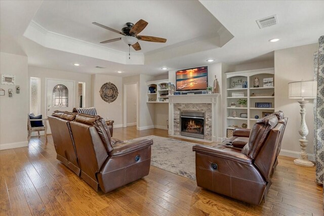 living area with a fireplace with flush hearth, a tray ceiling, visible vents, a ceiling fan, and crown molding