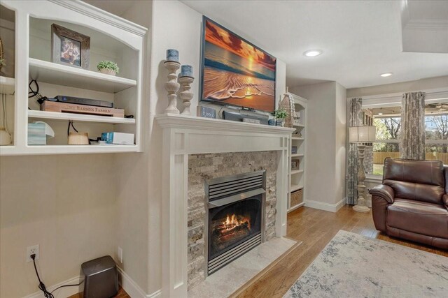 living room featuring baseboards, recessed lighting, built in features, wood finished floors, and a high end fireplace