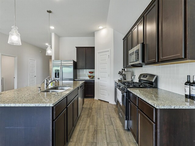 kitchen with stainless steel appliances, wood finished floors, a sink, a center island with sink, and dark brown cabinetry
