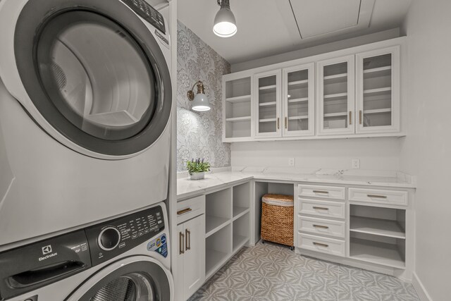 clothes washing area with cabinet space, stacked washer and dryer, and wallpapered walls