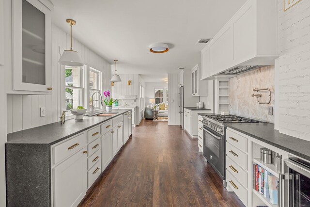 kitchen featuring high end appliances, dark countertops, a sink, decorative backsplash, and dark wood-style flooring