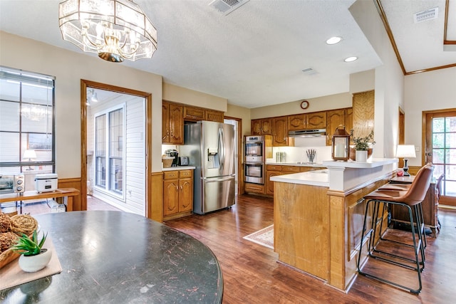 kitchen with under cabinet range hood, stainless steel appliances, visible vents, a peninsula, and brown cabinetry