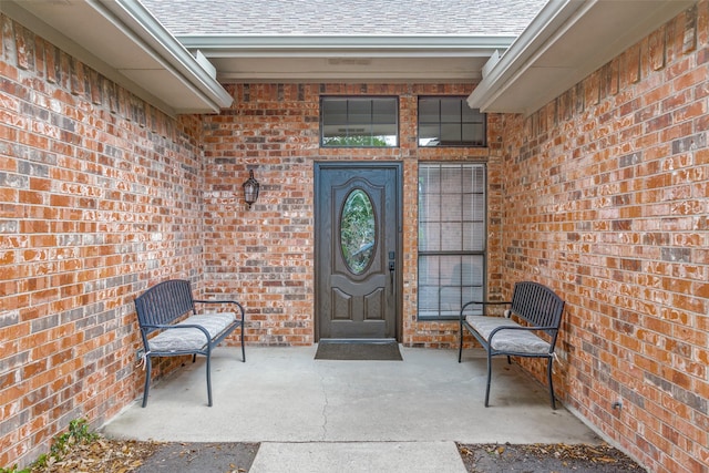 entrance to property featuring a shingled roof and brick siding