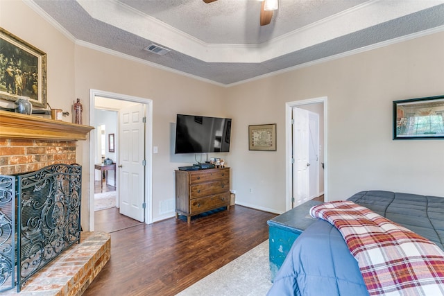 bedroom with a raised ceiling, wood finished floors, visible vents, ornamental molding, and a textured ceiling