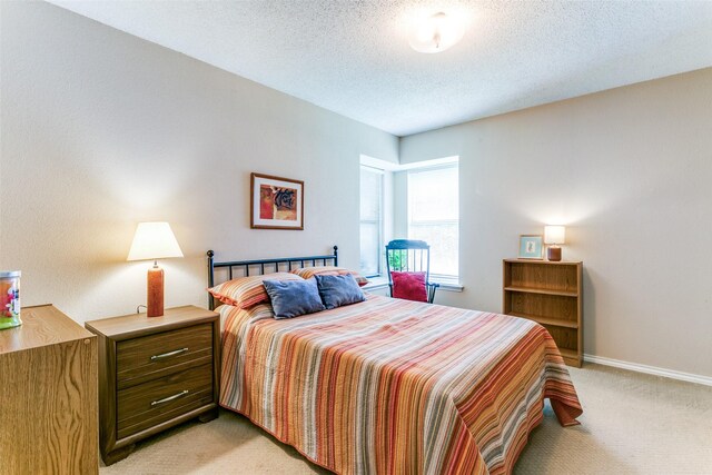 bedroom featuring light colored carpet, baseboards, and a textured ceiling