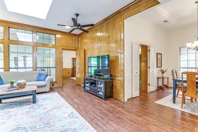 living area with visible vents, ceiling fan with notable chandelier, wood finished floors, a decorative wall, and ornamental molding