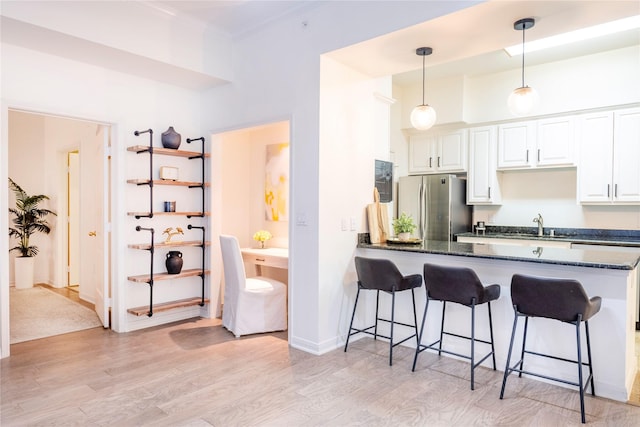 kitchen with freestanding refrigerator, a kitchen breakfast bar, light wood-style flooring, a peninsula, and ornamental molding