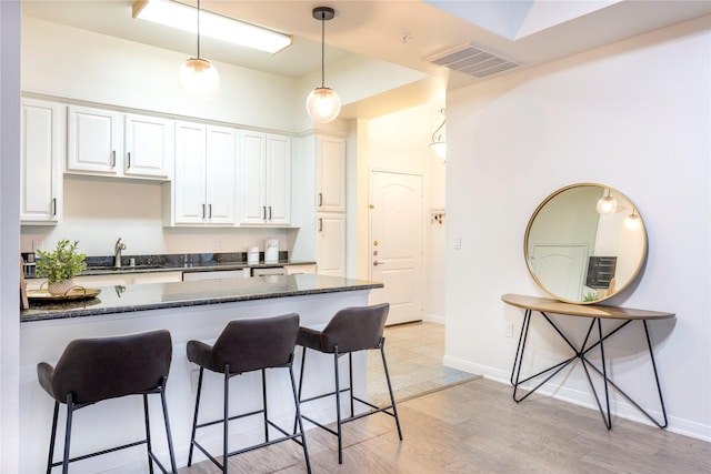 kitchen featuring a sink, a breakfast bar, white cabinetry, and decorative light fixtures