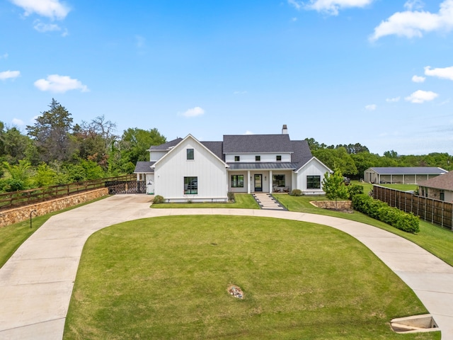 modern farmhouse style home featuring a chimney, fence, a front lawn, curved driveway, and board and batten siding