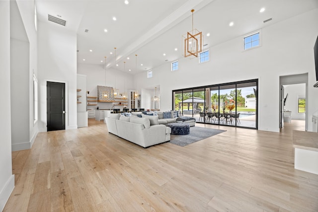 living area featuring light wood finished floors, a high ceiling, a notable chandelier, visible vents, and recessed lighting