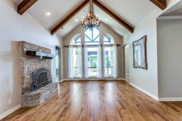 unfurnished living room with beamed ceiling, wood finished floors, a stone fireplace, arched walkways, and a chandelier