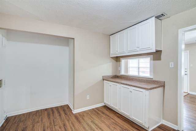 kitchen with white cabinets, baseboards, wood finished floors, and visible vents