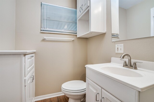 bathroom featuring baseboards, wood finished floors, toilet, and vanity