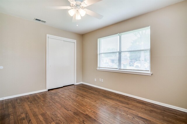 unfurnished bedroom featuring a ceiling fan, a closet, baseboards, dark wood-type flooring, and visible vents