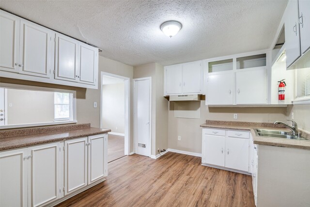 kitchen with light wood-type flooring, baseboards, white cabinetry, and a sink