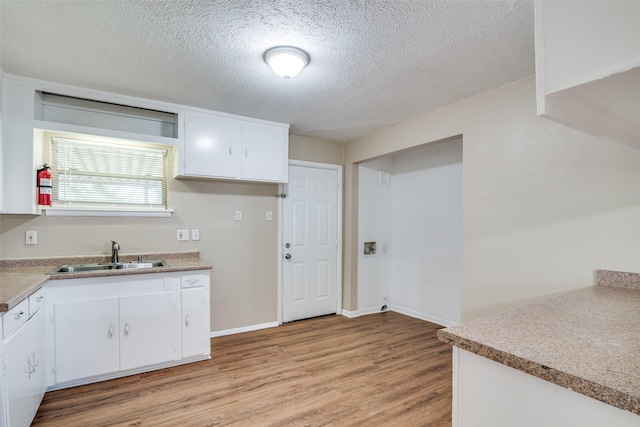 kitchen with a sink, a textured ceiling, light wood-style flooring, light countertops, and white cabinets