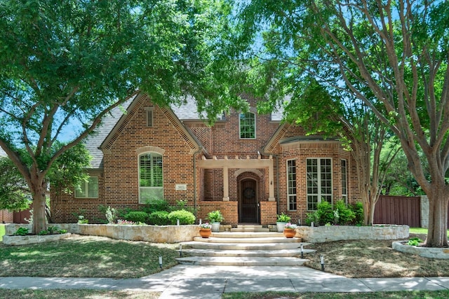 tudor house with fence, a shingled roof, and brick siding