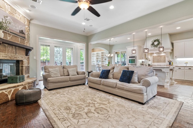 living area with a large fireplace, a ceiling fan, crown molding, and visible vents
