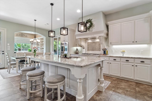 kitchen featuring white cabinets, a chandelier, decorative backsplash, a breakfast bar, and an island with sink